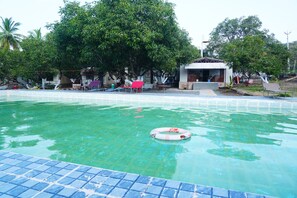 Una piscina con agua cristalina, rodeada de árboles y un pequeño edificio con techo.
