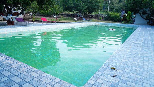 A rectangular swimming pool with clear water, surrounded by a tiled deck. - Kesar Villa (Bhojde)