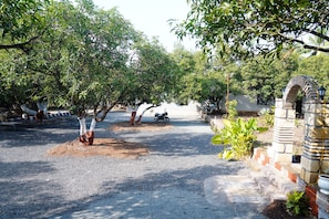 A paved driveway leading to a gated entrance with a stone archway, surrounded by lush greenery and trees.