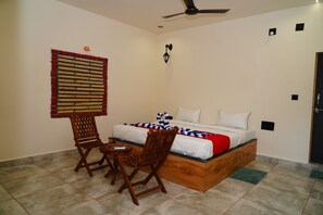A bedroom with a bed, two wooden chairs, a small table, a ceiling fan, and a wall-mounted light fixture. - Kesar Villa (Bhojde)