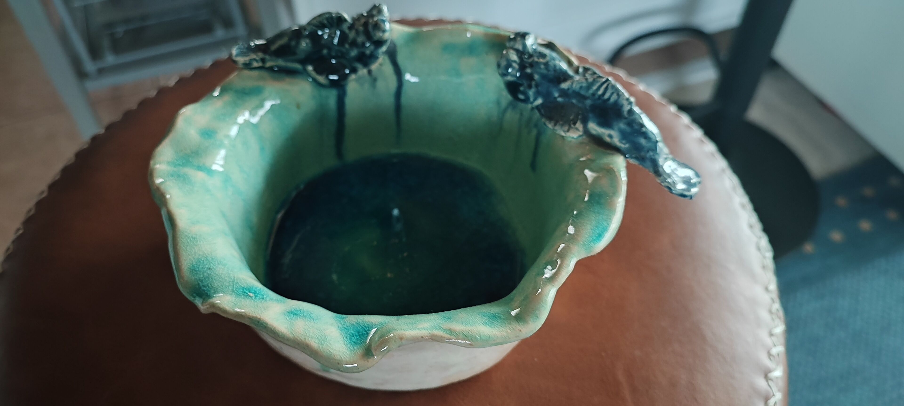 Un tazón de cerámica con esmaltado verde y azul, sobre una superficie de madera.