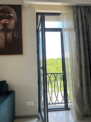 An open sliding door leading to a balcony with a view of greenery.