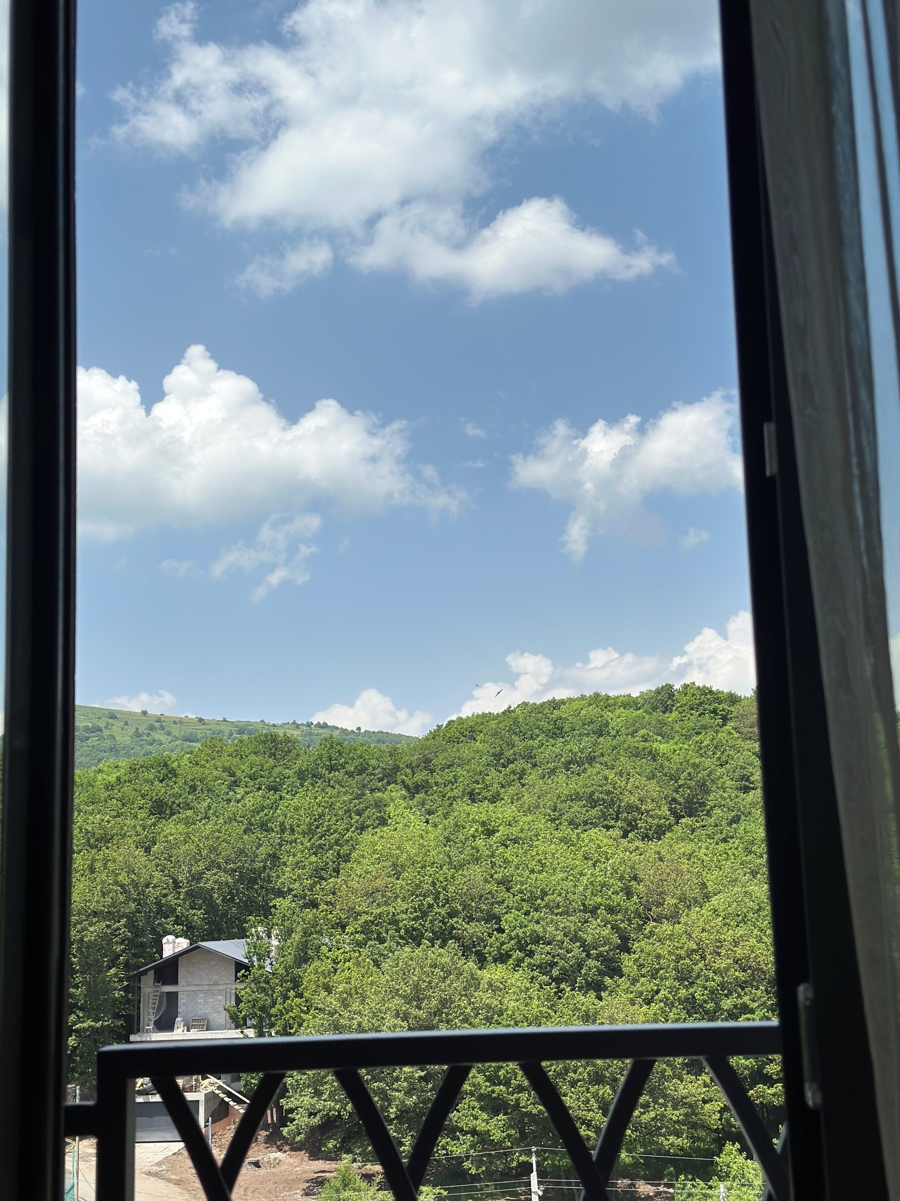 Vista através de uma janela de uma paisagem verde exuberante com céu claro.
