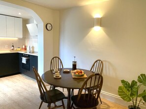 A dining area with a round table, four chairs, a bowl of fruit, and a clock on the wall. - The Cottage - Centre of Newcastle Co.Down (Newcastle)