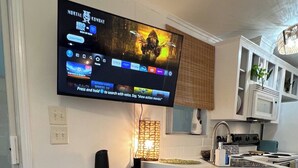 Una cocina moderna con televisor de pantalla plana sobre una encimera blanca, microondas integrado y estufa.
