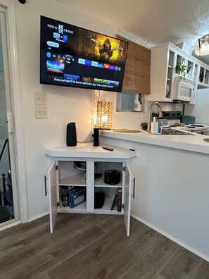 A modern kitchen with a flat-screen TV mounted above a white counter, a built-in microwave, and a stove.