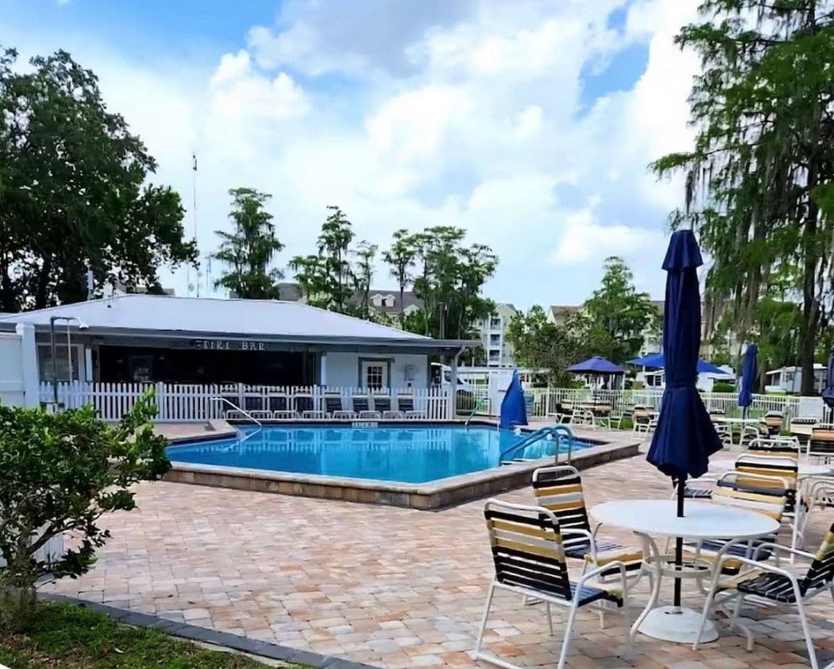 Un espace piscine avec des chaises longues et des parasols, un bar et une clôture blanche.