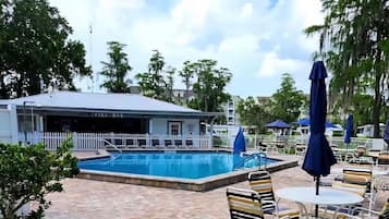 Un espace piscine avec des chaises longues et des parasols, un bar et une clôture blanche.