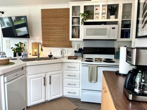 Une cuisine moderne avec des meubles blancs, une cuisinière, un four à micro-ondes et un téléviseur fixé au-dessus de l’évier.