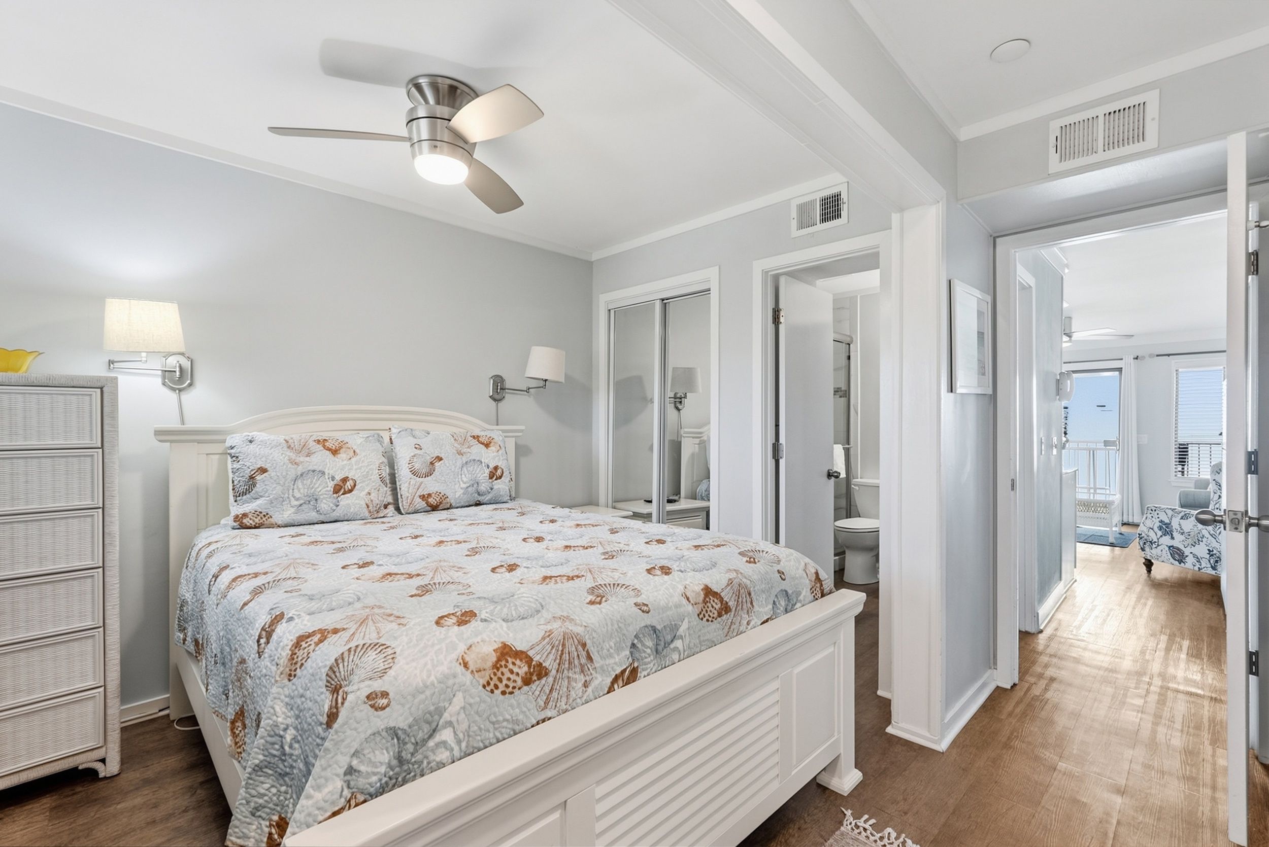 Un dormitorio con cama, ventilador de techo, cómoda y baño visible a través de una puerta abierta.
