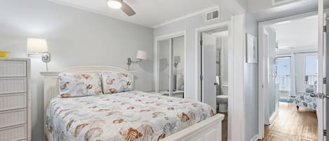Un dormitorio con cama, ventilador de techo, cómoda y baño visible a través de una puerta abierta.