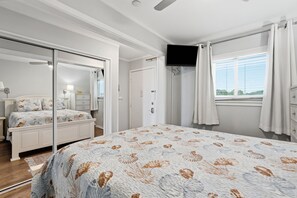 Un dormitorio con cama, espejo, televisor y ventana con cortinas.