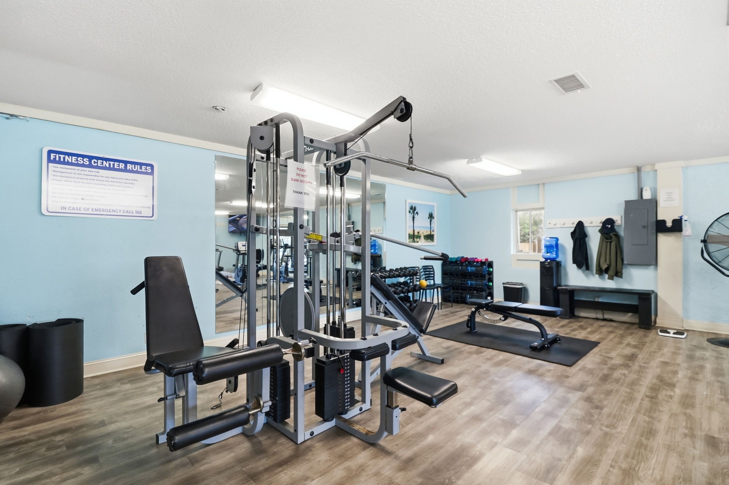 Un gimnasio con equipo de ejercicio, un cartel con normas y un dispensador de agua.