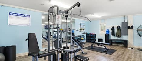 Un gimnasio con equipo de ejercicio, un cartel con normas y un dispensador de agua.