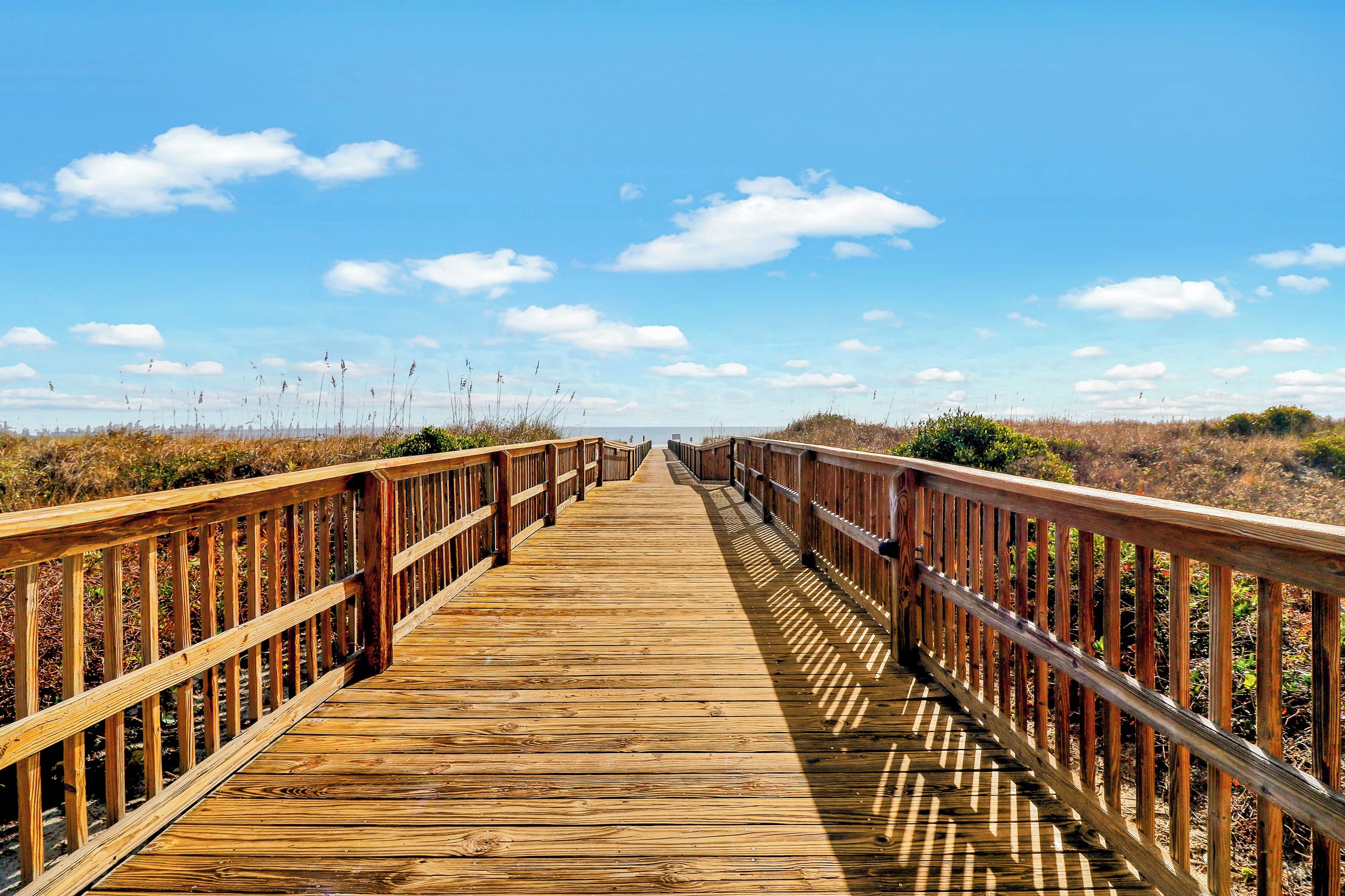 A wooden boardwalk leading to a beach with a clear sky.