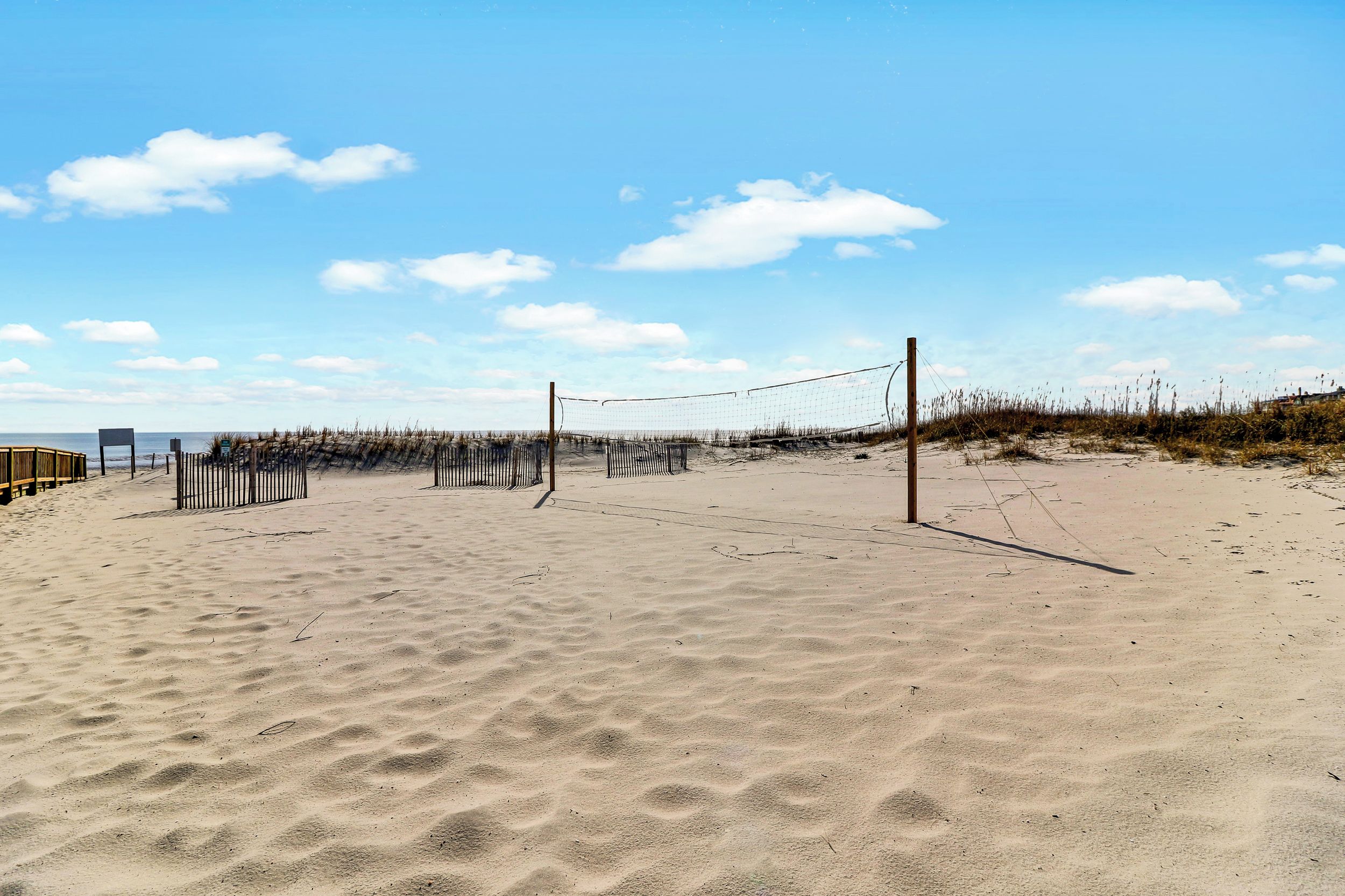 Una cancha de voleibol de playa con red, arena y vegetación escasa.
