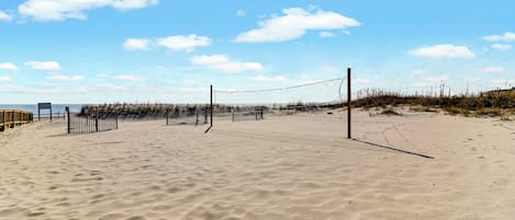 Una cancha de voleibol de playa con red, arena y vegetación escasa.