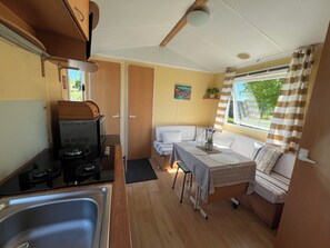 A compact RV kitchen with a stove, sink, and a small dining area with a table and seating. - Mobile Home in the Countryside (Juillac)