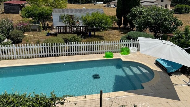 Ein Swimmingpool mit weißem Zaun, umgeben von Bäumen und einem kleinen Gebäude.