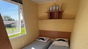 Ein kleines Zimmer mit zwei Betten, einem Fenster und einem kleinen Regal mit Dekoration.