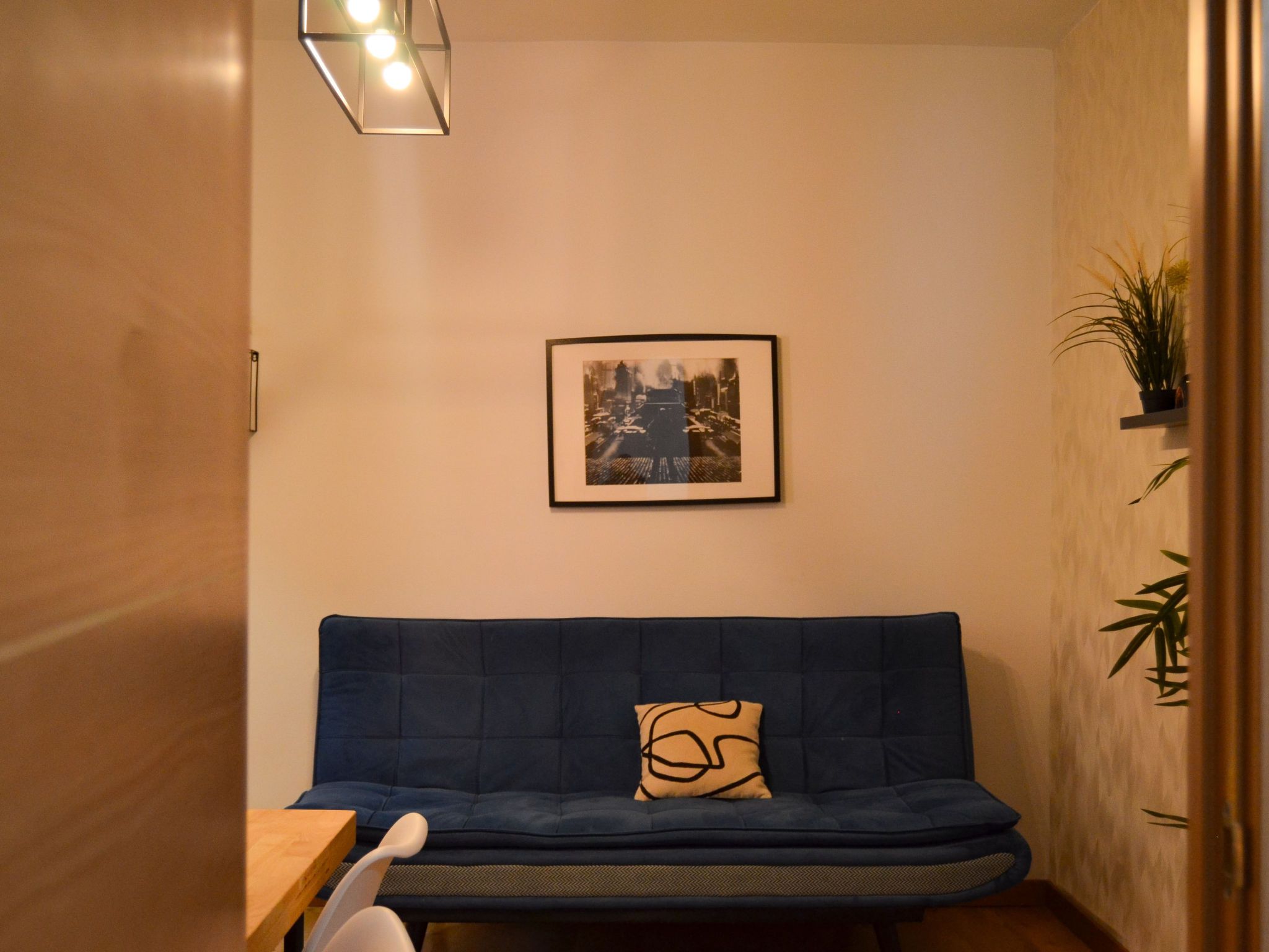 Una habitación con un sofá azul, un cuadro en la pared y una pequeña mesa con una silla.