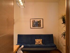 A room with a blue sofa, a framed picture on the wall, and a small table with a chair. - Apartment  by Interhome (Madrid)