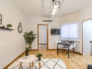 Un soggiorno moderno con zona pranzo, una TV montata a parete e una porta che conduce in un'altra stanza.