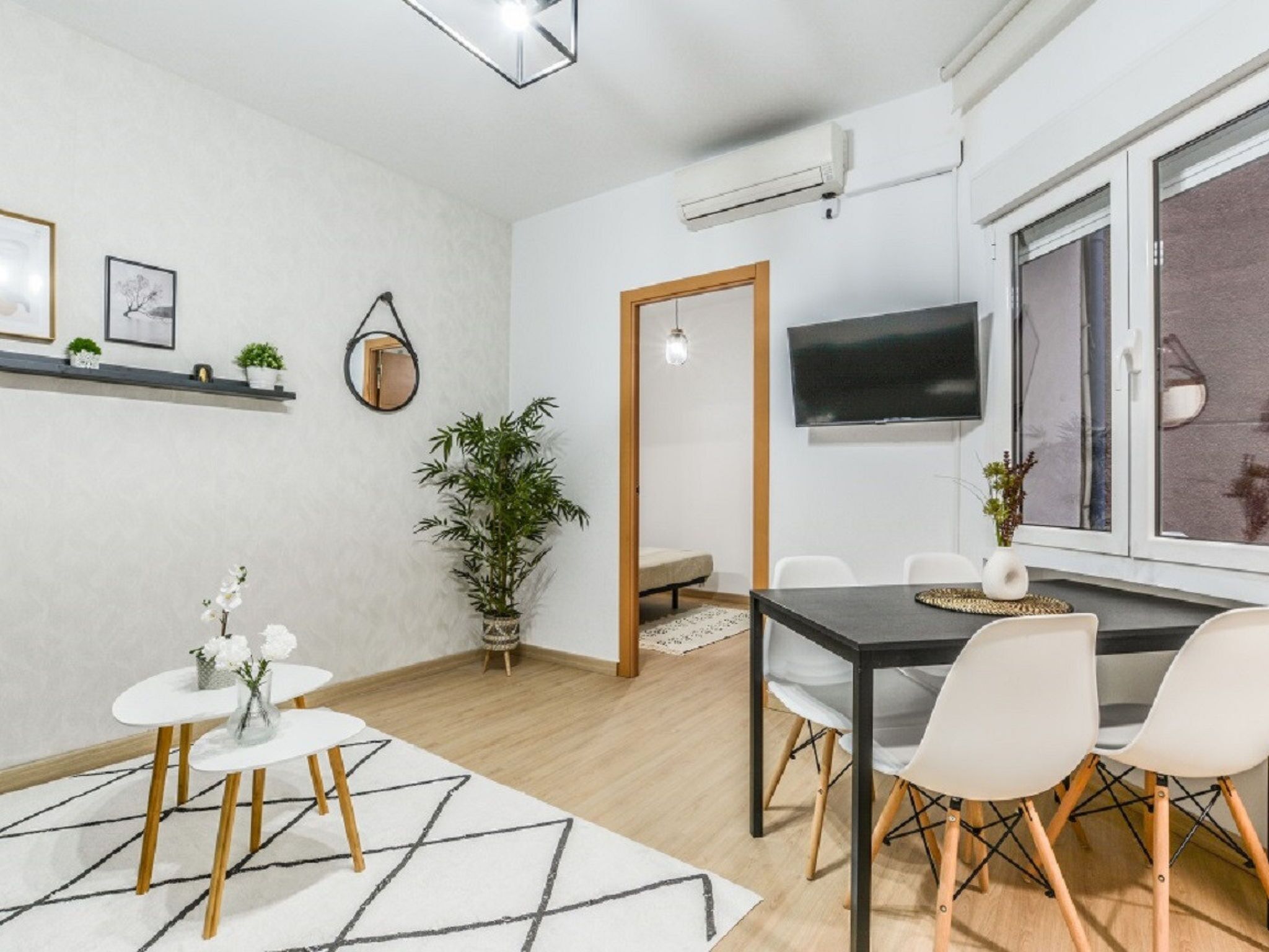 Una sala de estar moderna con comedor, televisor montado en la pared y un ventanal grande.