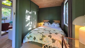 A bedroom with a bed, a nightstand, a window, and a view of greenery outside.