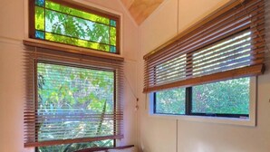 A room with a wooden ceiling, a sofa with cushions, and two windows with blinds.