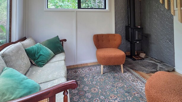 A cozy room with a sofa, a chair, a patterned rug, a window, and a wood-burning stove.