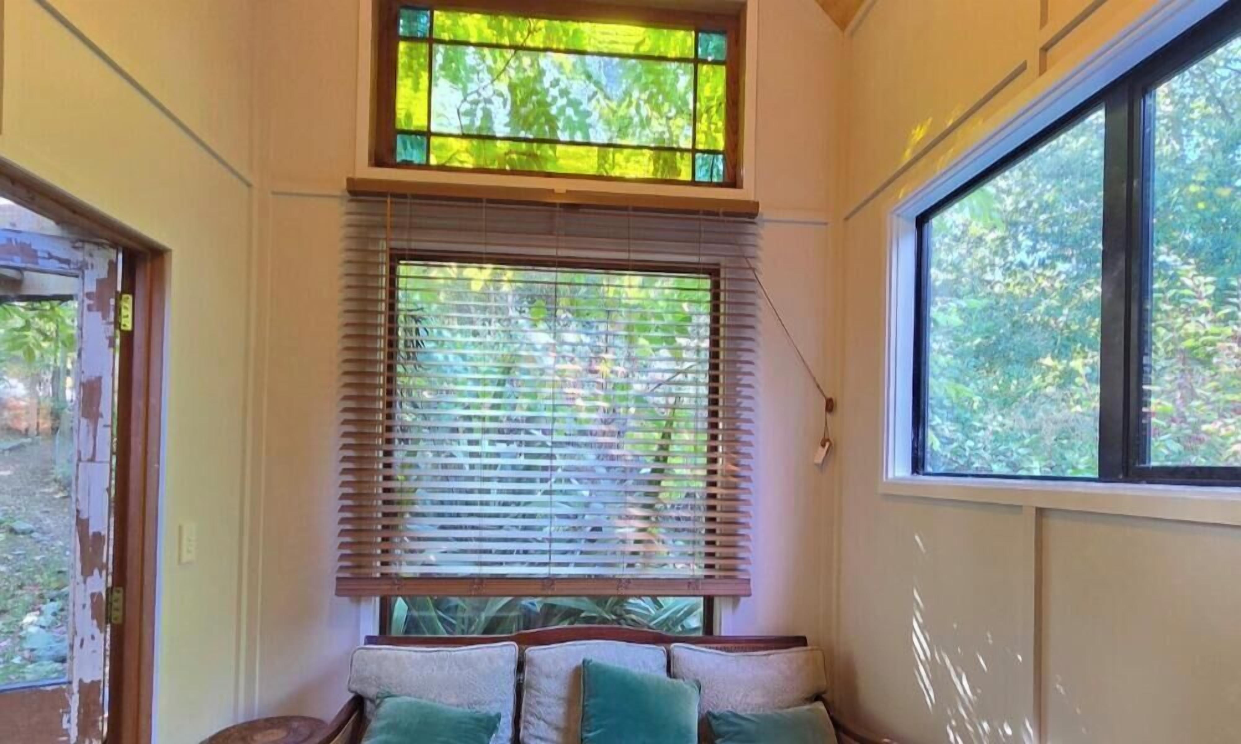 A room with a large window, a bench, and a view of greenery outside.