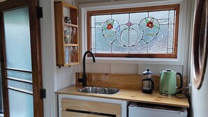 A compact kitchen with a wooden countertop, a stainless steel sink, a small refrigerator, and a window with a stained glass design.