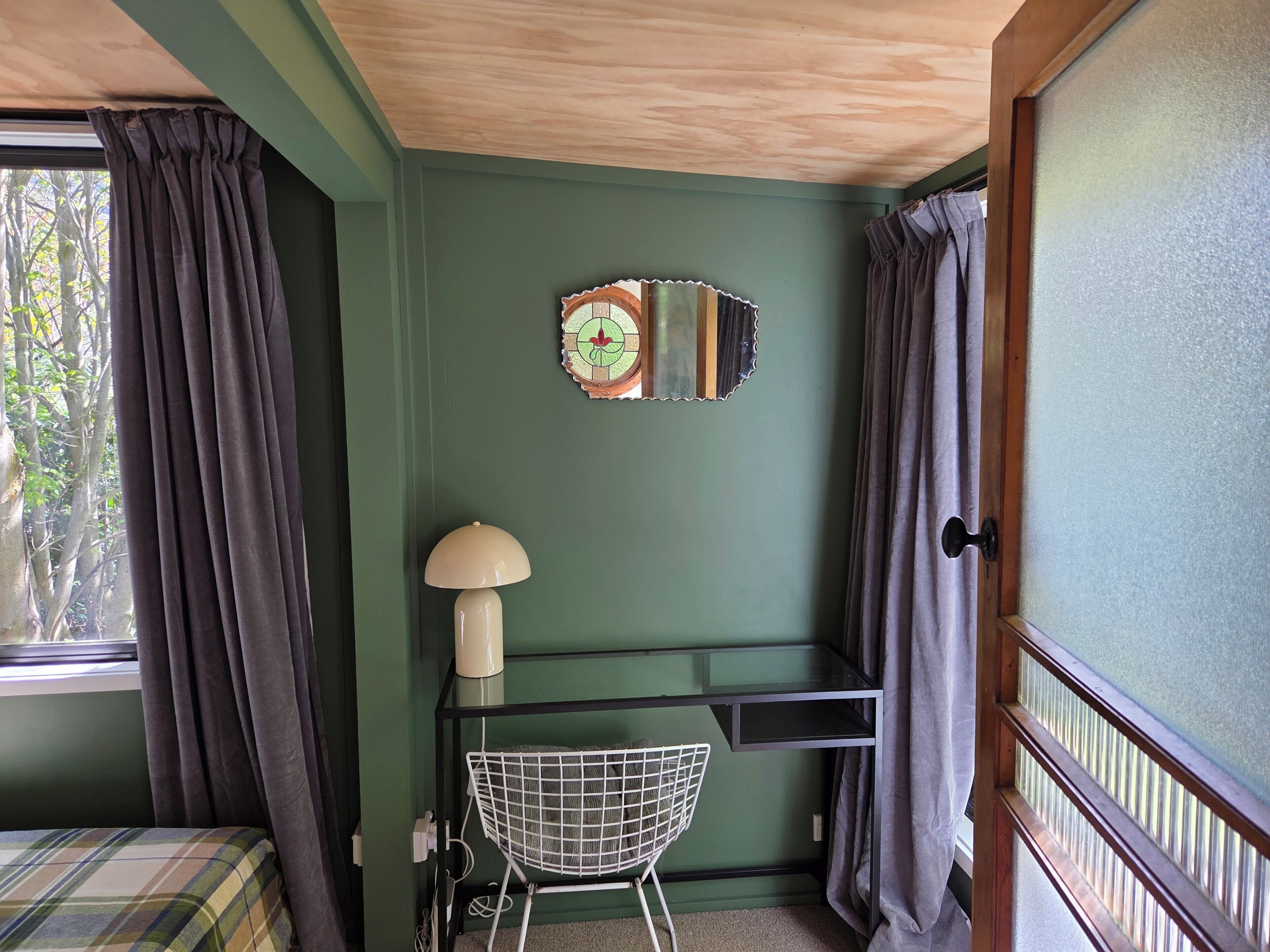 A room with a bed, a desk with a chair, a lamp, and a mirror on the wall.