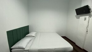 Een eenpersoonsbed met een groen hoofdeinde in een kleine, zwak verlichte kamer.