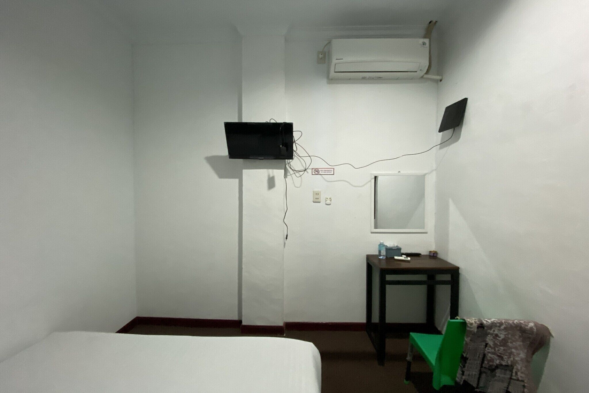 Una habitación con cama, una mesita de noche con espejo, aire acondicionado y un televisor en la pared.