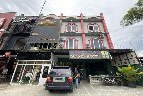 A building with a sign for 'Ratu House' and 'Quanza Hotel' with a car parked in front.