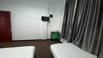 Ett hotellrum med två sängar, en tv på väggen, ett litet bord med en stol och en röd dörr.