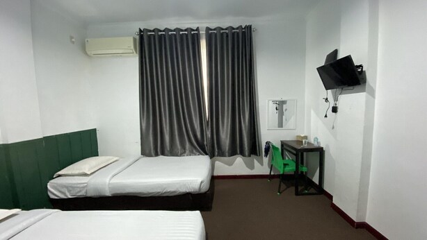 A hotel room with two beds, a desk, a chair, a TV, and curtains.