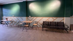 A room with a wooden floor, a table with chairs, a bench, and a green wall with a geometric pattern.