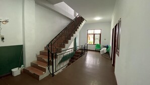 A hallway with a staircase, a window with curtains, and a green chair.