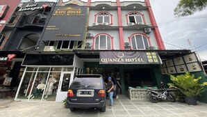 A building with a sign for 'Ratu House' and 'Quanza Hotel' with a car parked in front.