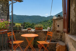 Eine Terrasse im Freien mit einer Steinmauer, einem Tisch, zwei Stühlen und Topfpflanzen.
