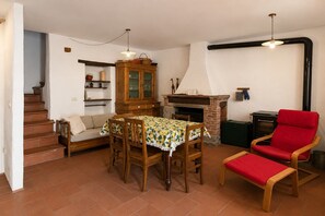 Ein Essbereich mit einem Tisch für vier Personen, einem roten Sessel, einem Kamin und einer Treppe, die zu einer oberen Etage führt.