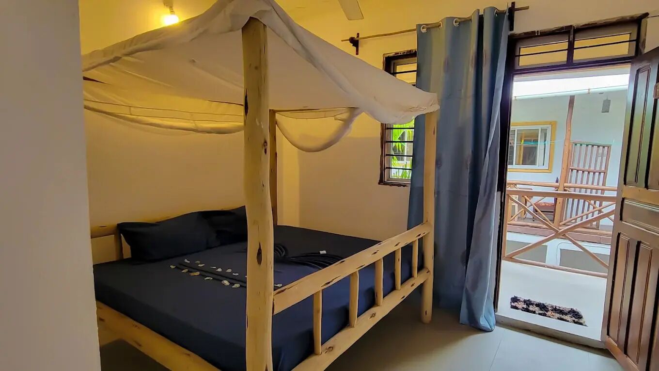 A single bed with a canopy, a window with a view of the outside, and a door leading to a balcony.