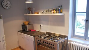 Een praktische keuken met een magnetron, fornuis en vaatwasser. Op de muur hangt een klok en er is een raam met uitzicht.