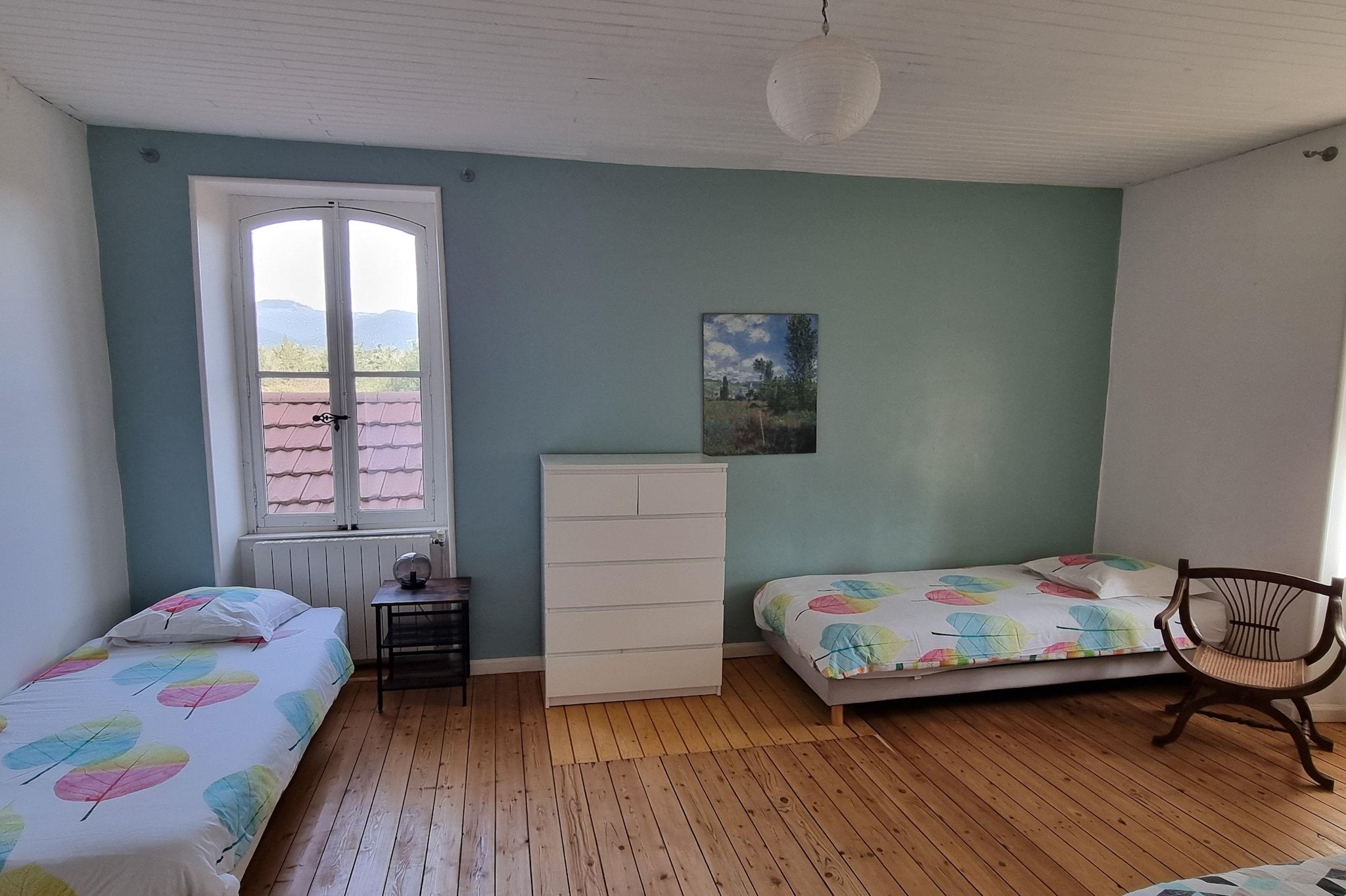 Ein Schlafzimmer mit zwei Betten, einem Schminktisch, einem Stuhl, einem Fenster und einem Bild an der Wand.