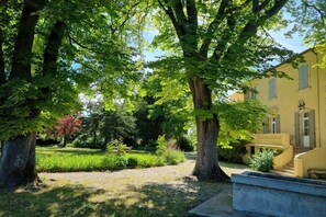 Ein Garten mit Bäumen und einem gelben Gebäude mit einer Treppe.