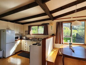 A compact kitchen with a refrigerator, microwave, stove, and wooden counter. - Classic Kiwi Oceanview Bach (Hahei)