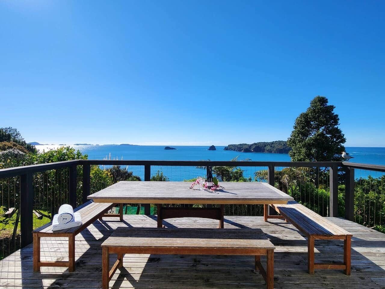 Une terrasse en bois avec une table et des bancs donnant sur une étendue d’eau.
